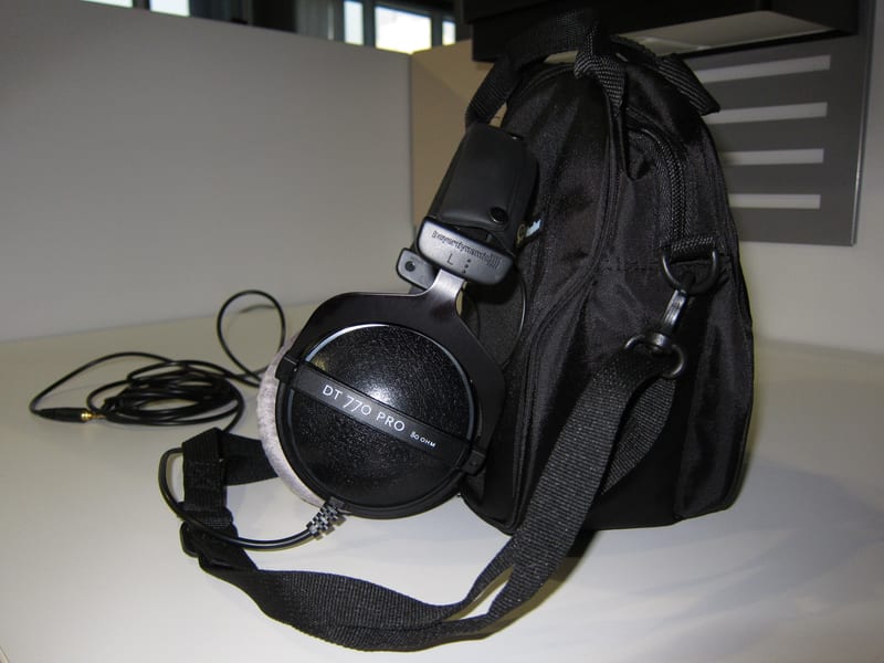 Beyerdynamic DT 770 Pro 80 ohm closed-back headphones in black with silver yoke arms and grey velour ear pads, resting on a desk beside a carry bag